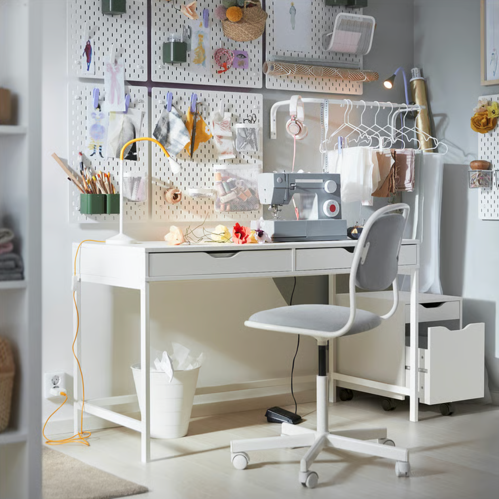 Sewing station with a machine, fabric samples, and craft supplies on a white desk and chair.