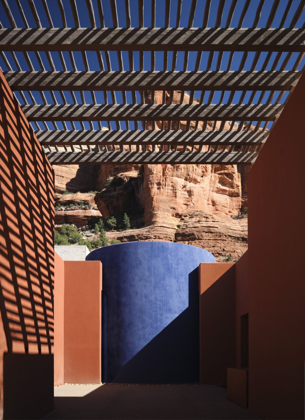 Shadowed pergola view with blue wall and red rock cliff in the background.
