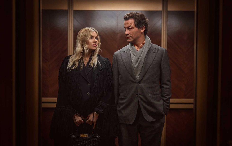 Sienna Miller and Dominic West people stand in an elevator, facing each other, wearing formal attire.