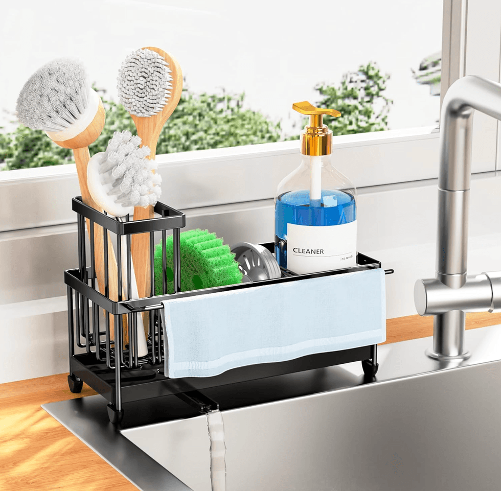 Sink caddy with brushes, sponge, soap dispenser, and towel by a window.