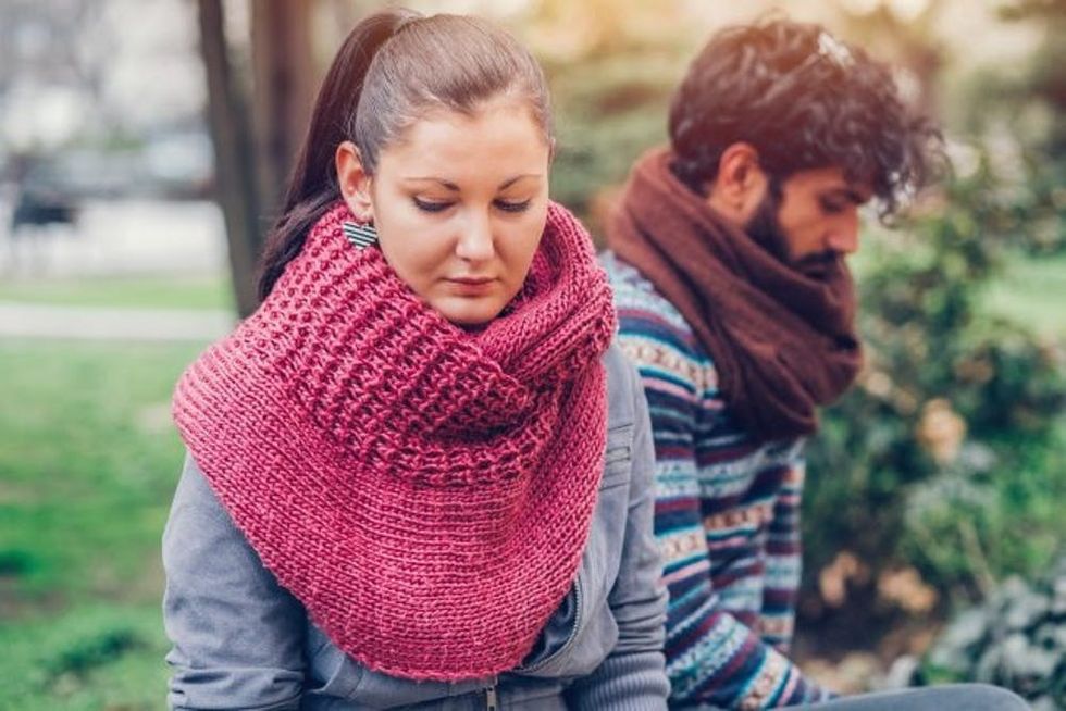 Sitting in a park, a woman sadly faces away from a man