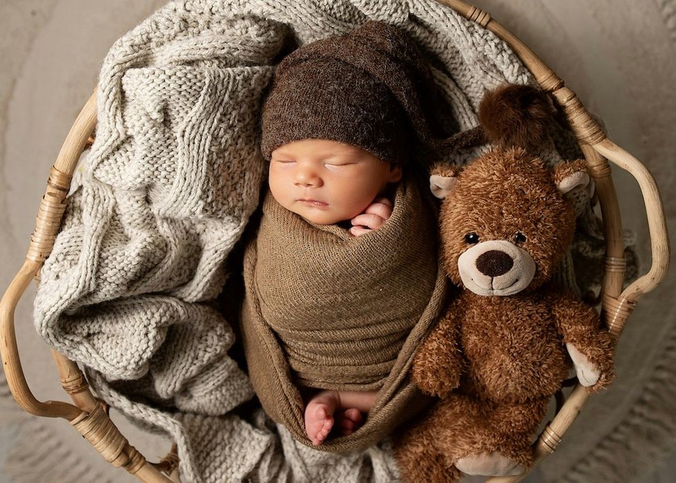 sleeping baby in a basket with a teddy bear