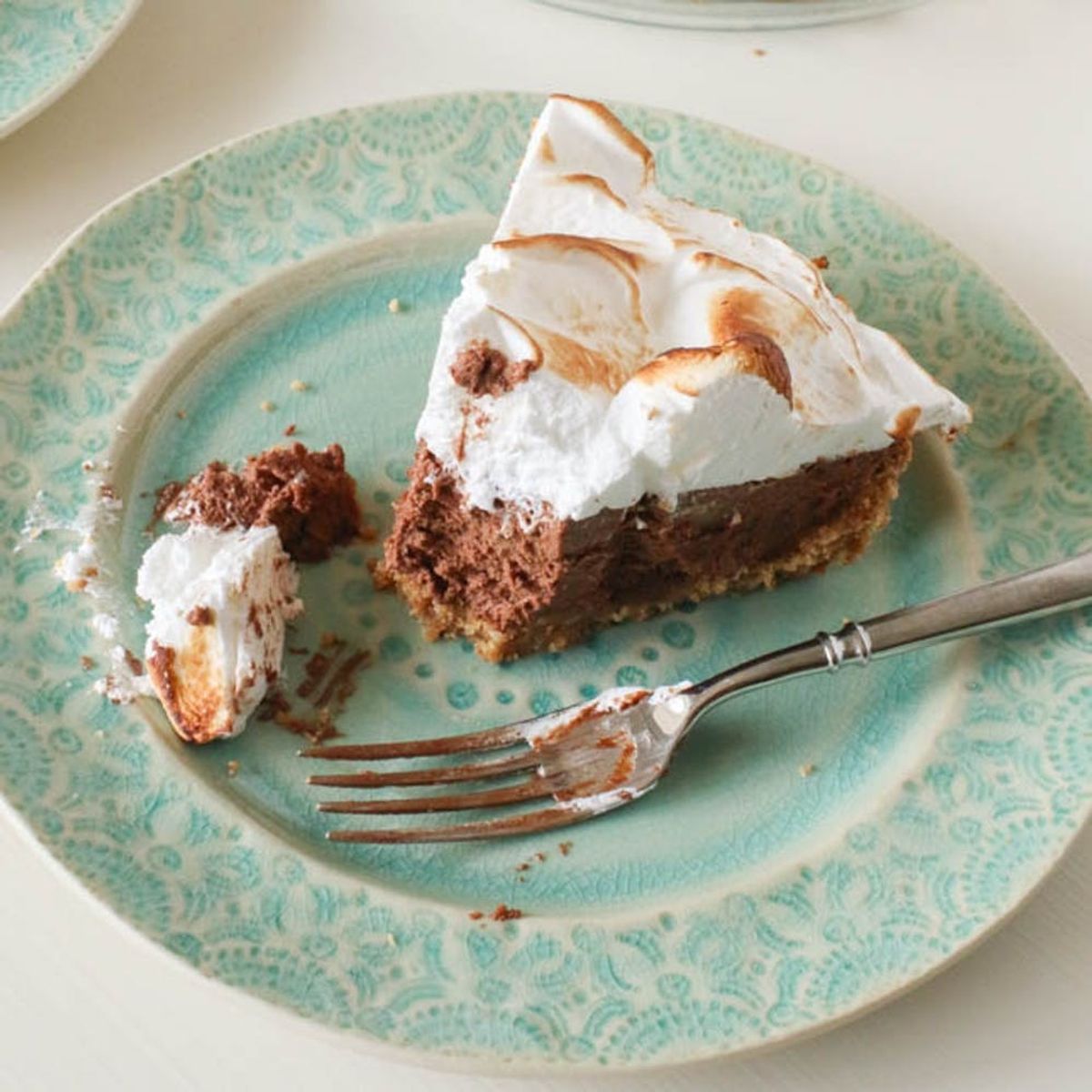 Slice of chocolate pie with meringue topping on a decorative turquoise plate, fork beside it.