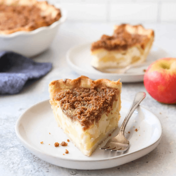 Slice of crumb-top apple pie on a plate with a fork and an apple nearby.
