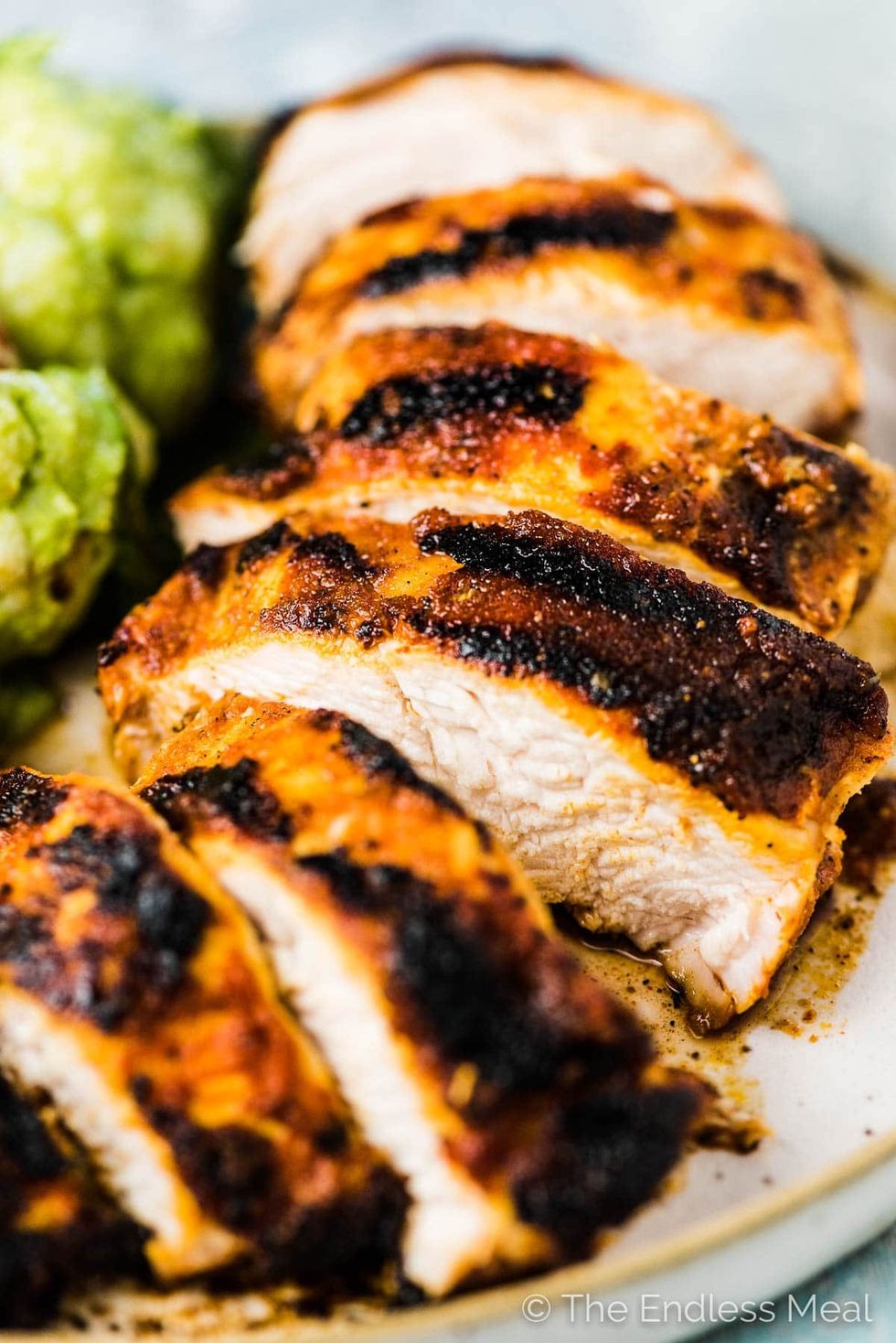 Sliced pieces of juicy chicken breast are next to greens.