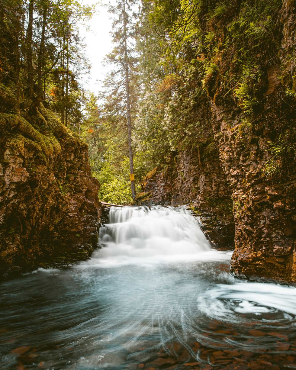 Small waterfall flowing through a lush, rocky forest canyon.