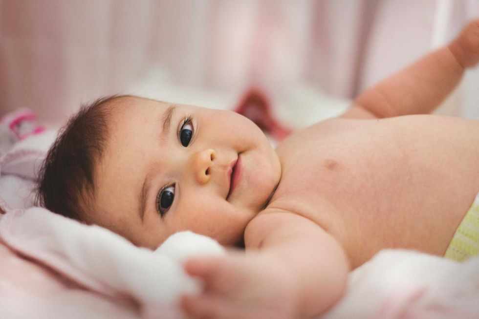 Smiling baby lying down, reaching out with arm, on a soft blanket.