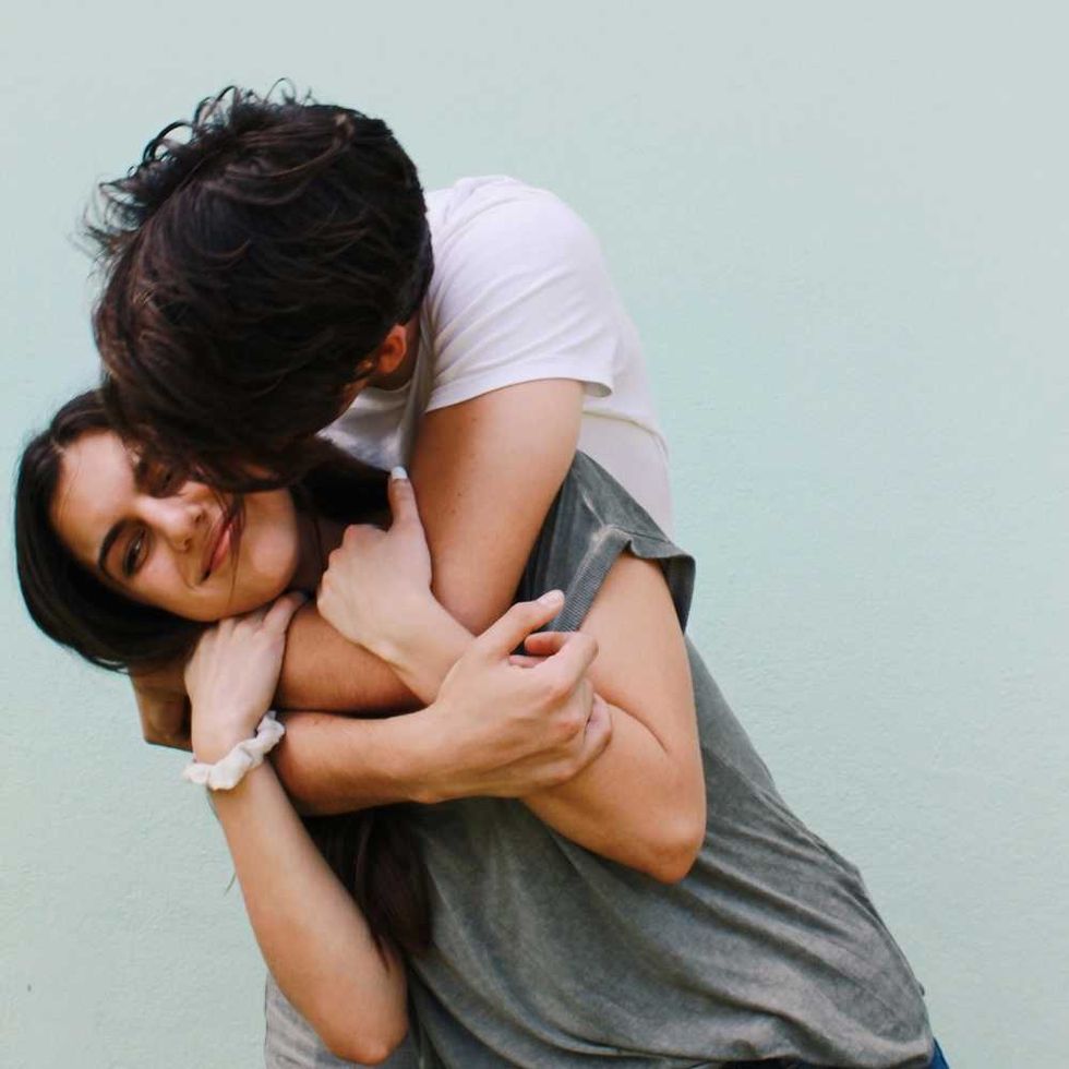 Smiling couple embracing playfully against a light blue background.