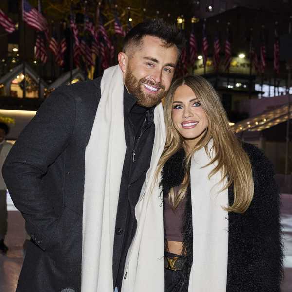 Smiling couple in scarves at a festive outdoor event with flags in the background.