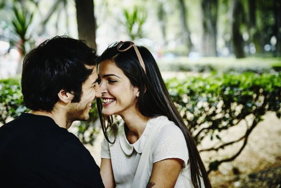 Smiling couple sitting in park leaning in to kiss