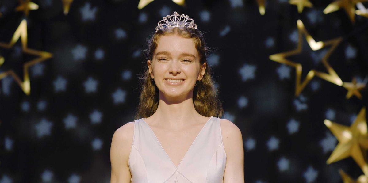 Smiling girl wearing a tiara, with star-shaped decorations in the background.