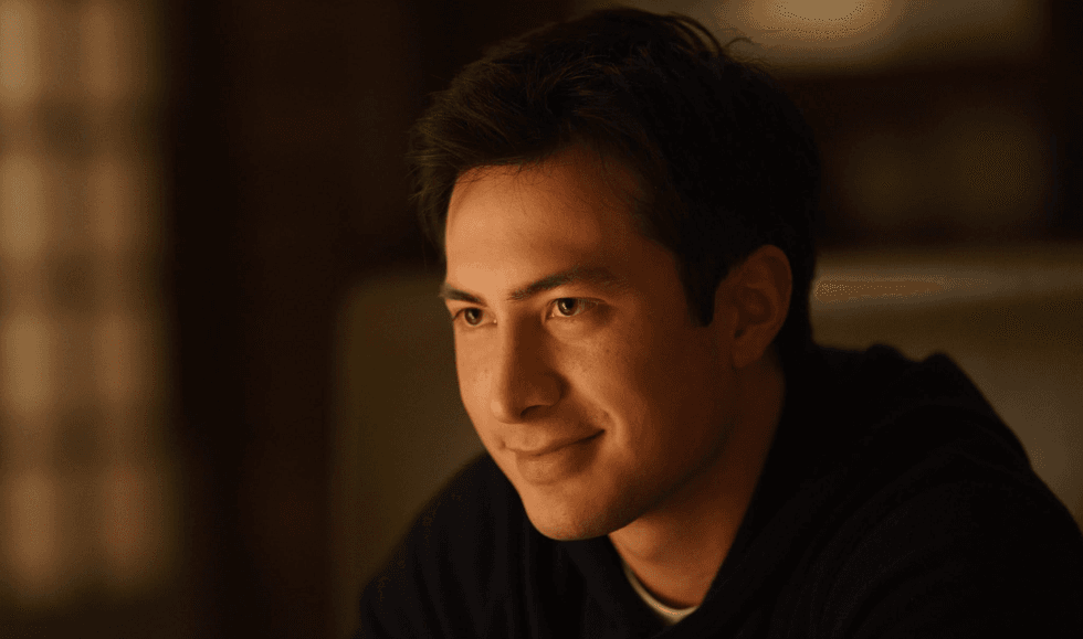 Smiling man in dimly lit room, looking thoughtfully to the side.