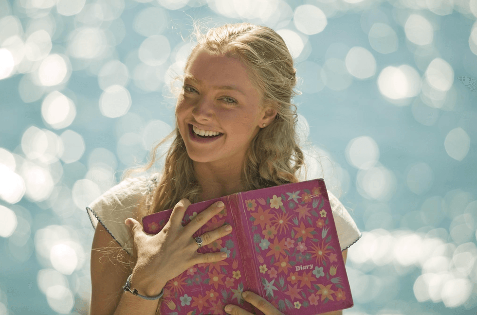 Smiling woman holding a diary against a sparkling water backdrop.