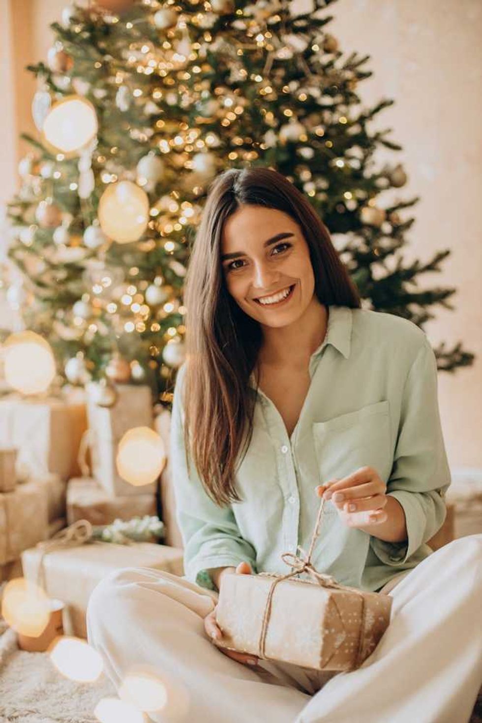 Smiling woman holding a gift by a decorated Christmas tree.