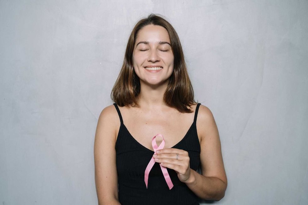 Smiling woman holding a pink ribbon, eyes closed in a black top.
