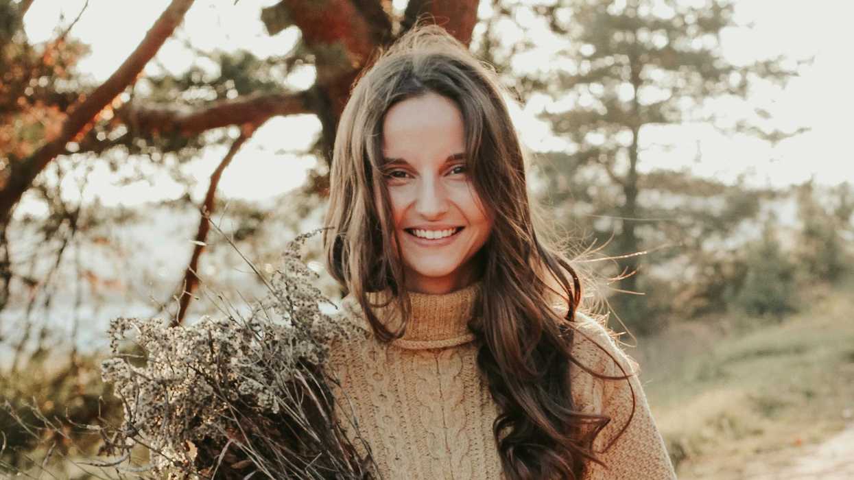 Smiling woman in a cozy sweater holding dried flowers outdoors in warm sunlight.