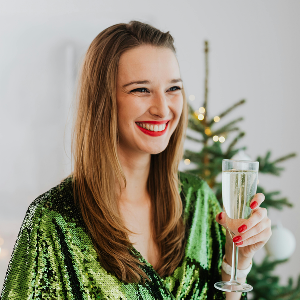 Smiling woman in a green dress holding a champagne flute near a Christmas tree.