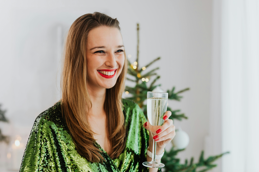 Smiling woman in a green dress holding a champagne flute near a Christmas tree.