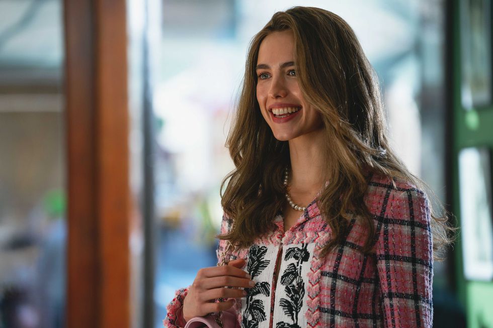 Smiling woman in a pink plaid jacket, standing indoors.