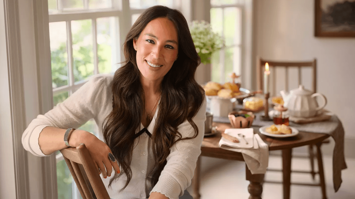 Smiling woman in cozy room seated by a table with tea and pastries.