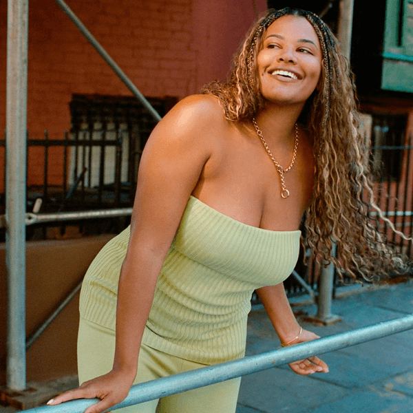 Smiling woman in green dress, leaning on a railing outdoors.