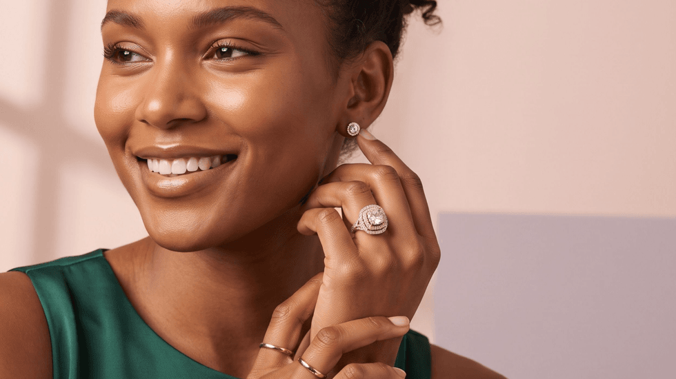 Smiling woman wearing elegant jewelry, including rings and earrings, in a green top.