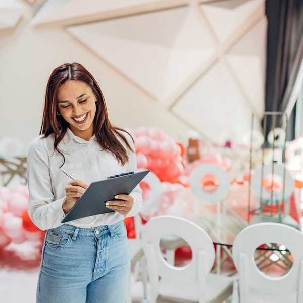 Smiling woman with clipboard stands in decorated room with pink and red balloons.