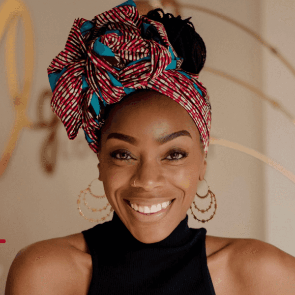 Smiling woman with colorful headwrap, large hoop earrings, and black top against a neutral background.