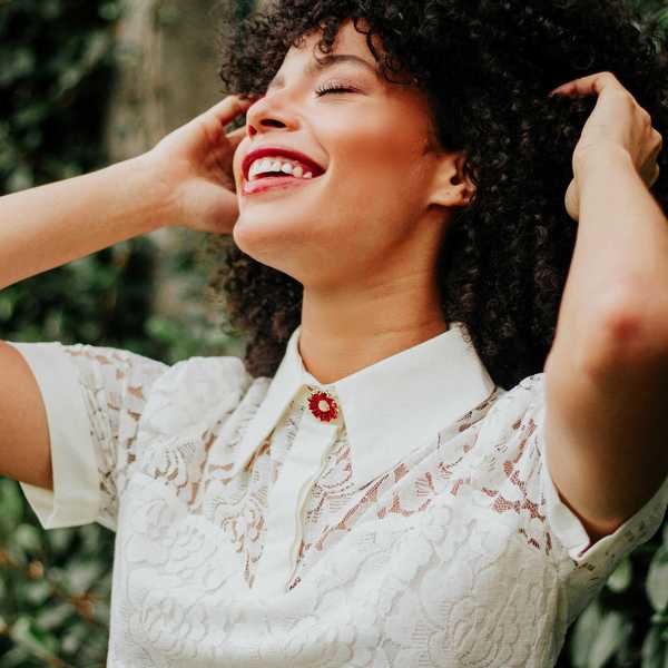 Smiling woman with curly hair, wearing a white lace dress, enjoying the outdoors.