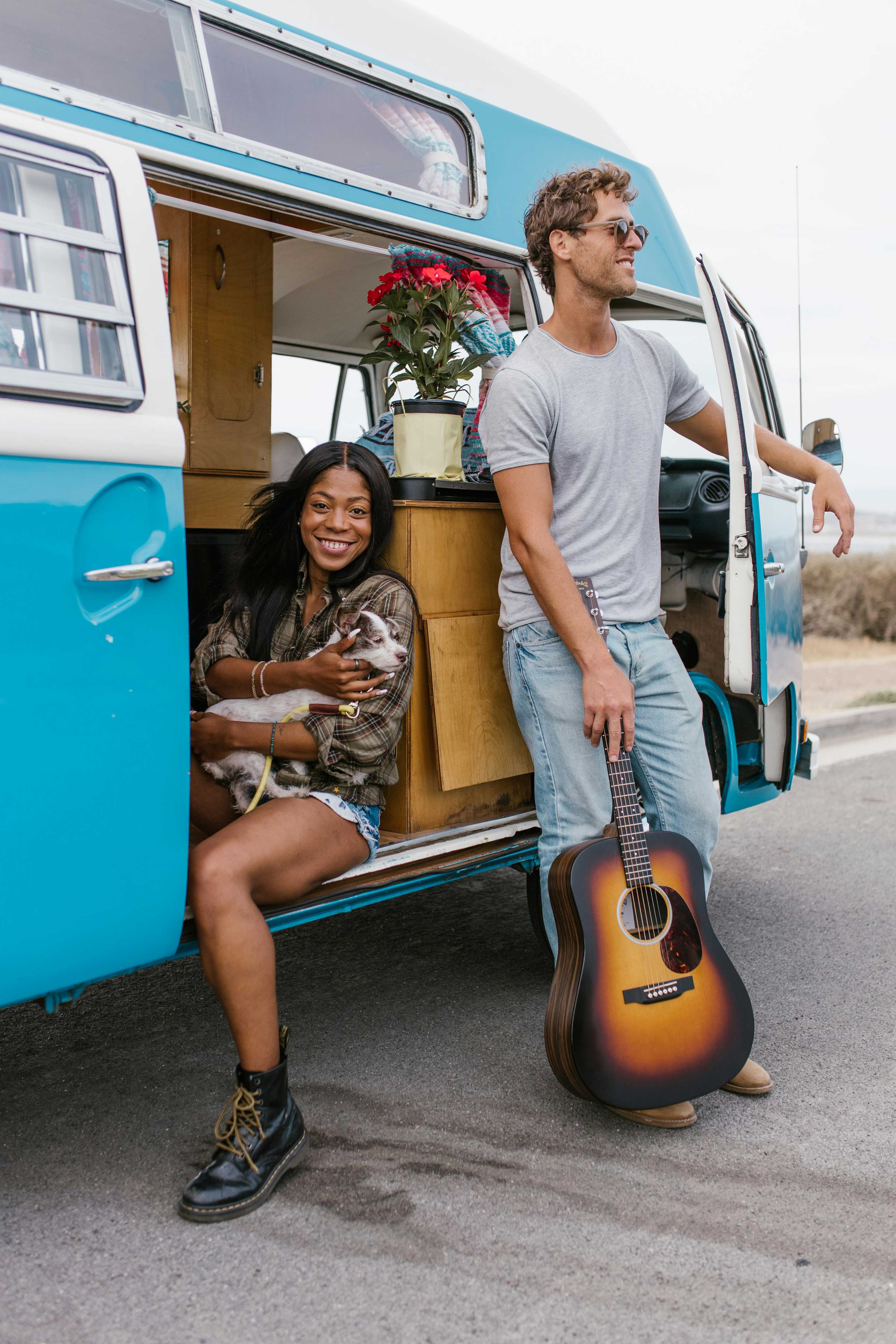 Smiling woman with dog in van doorway; man holding guitar, leaning on van.