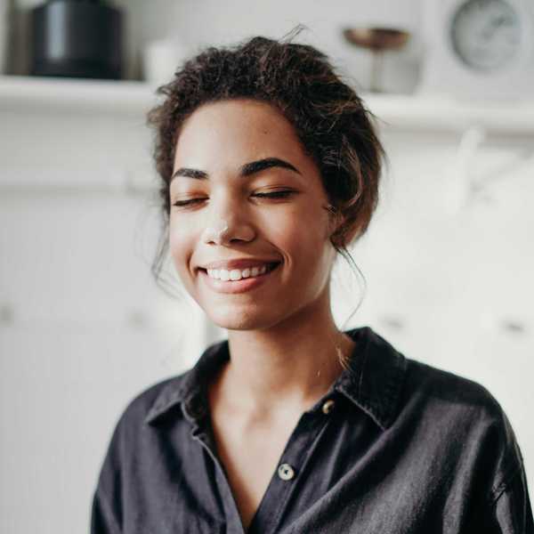 Smiling woman with eyes closed, wearing a black shirt in a softly lit room.