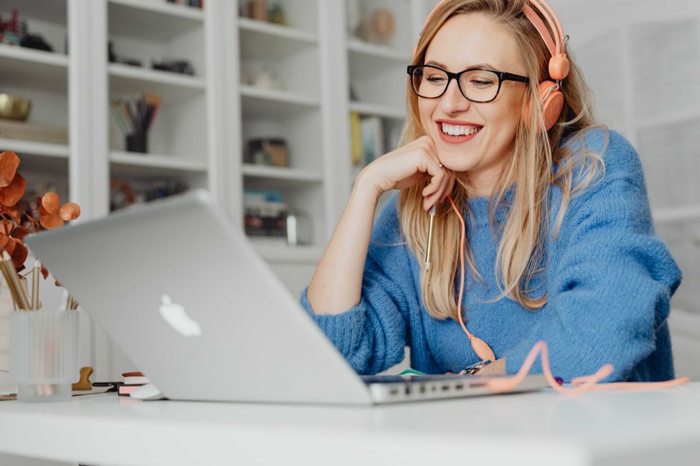 Smiling woman with headphones using a laptop at home office desk.
