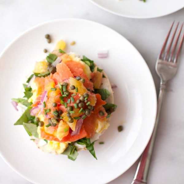 Smoked salmon bagel with cream cheese, capers, and veggies on a white plate.