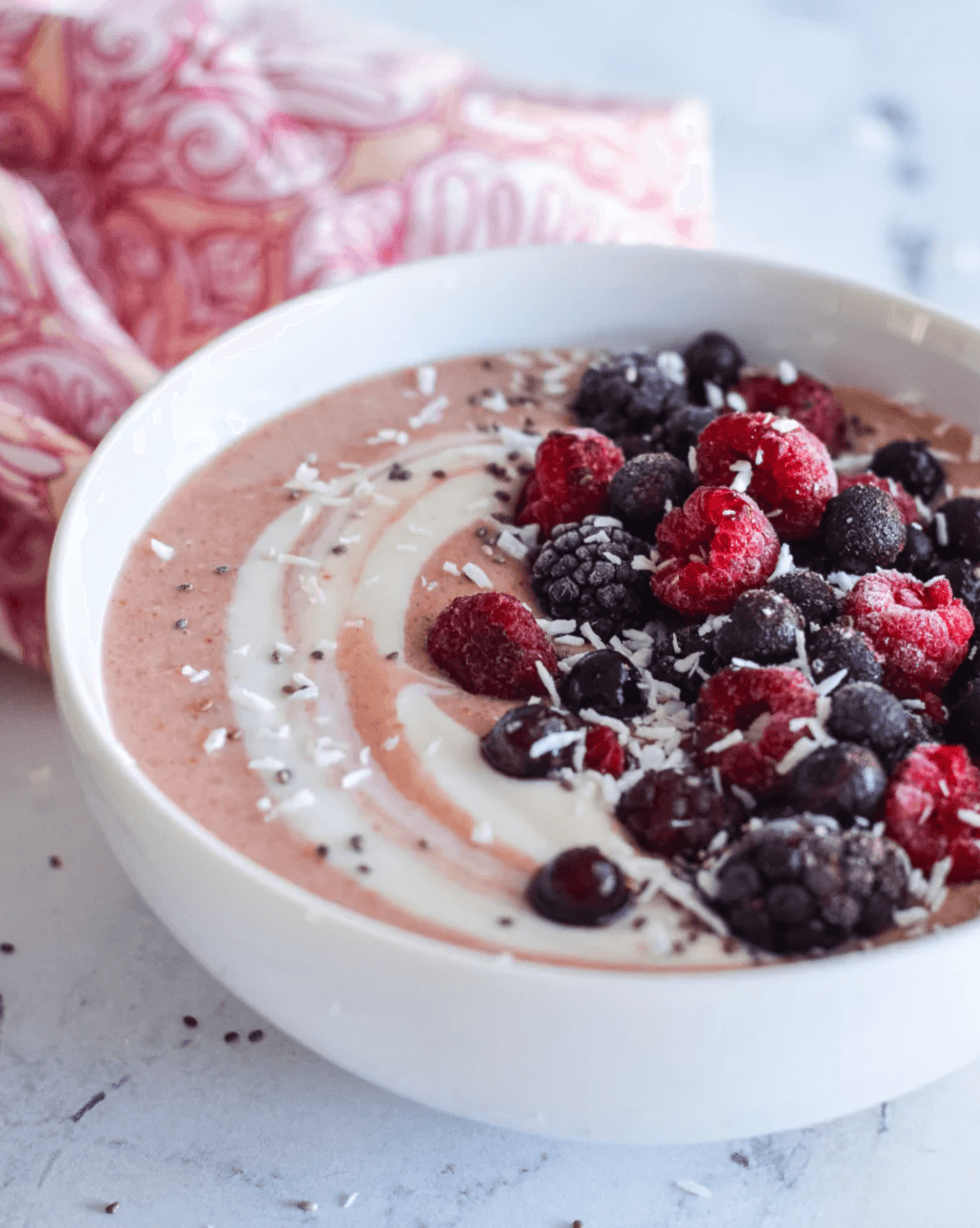 Smoothie bowl with berries, yogurt swirls, and coconut shavings on a white surface.