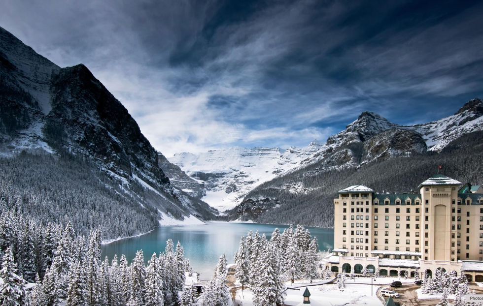 Snowy mountains, turquoise lake, and a grand hotel under a dramatic sky.