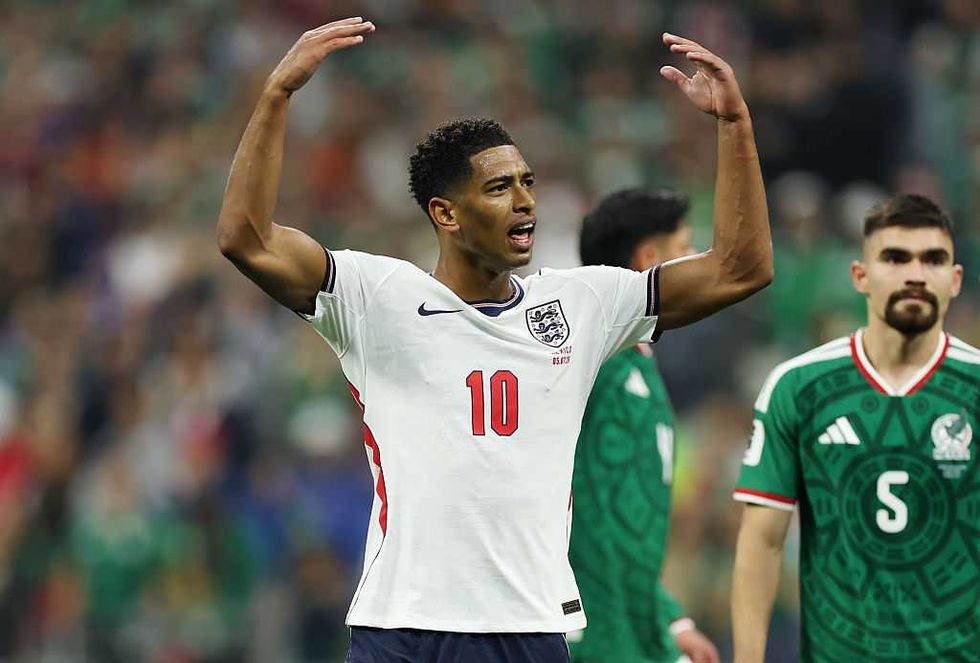 Soccer player in white jersey raising arms on the field, surrounded by opponents in green jerseys.