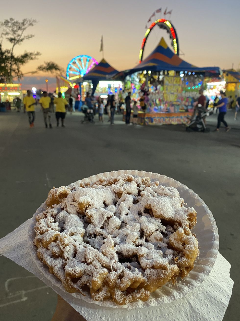 someone holding a plate of funnel cake at a local fair