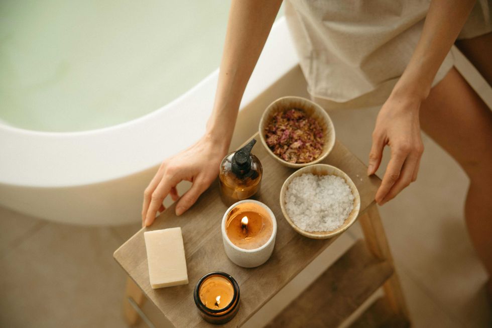 Spa setup with candles, bath salts, soap, and dried flowers by a bathtub.