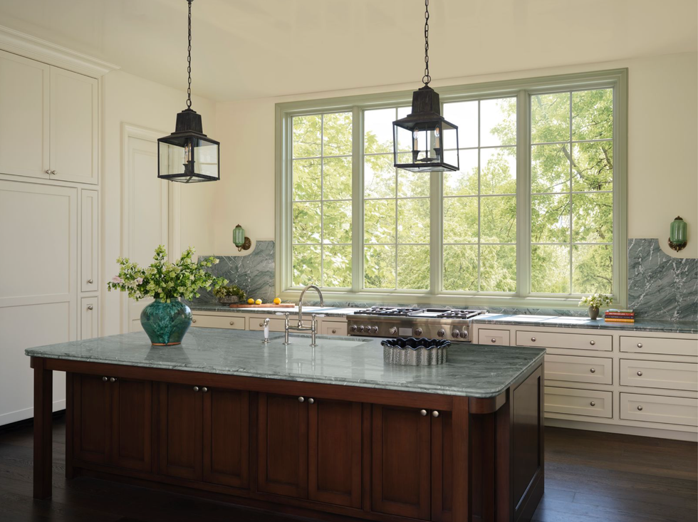 Spacious kitchen with large windows, island, green countertop, and pendant lights.