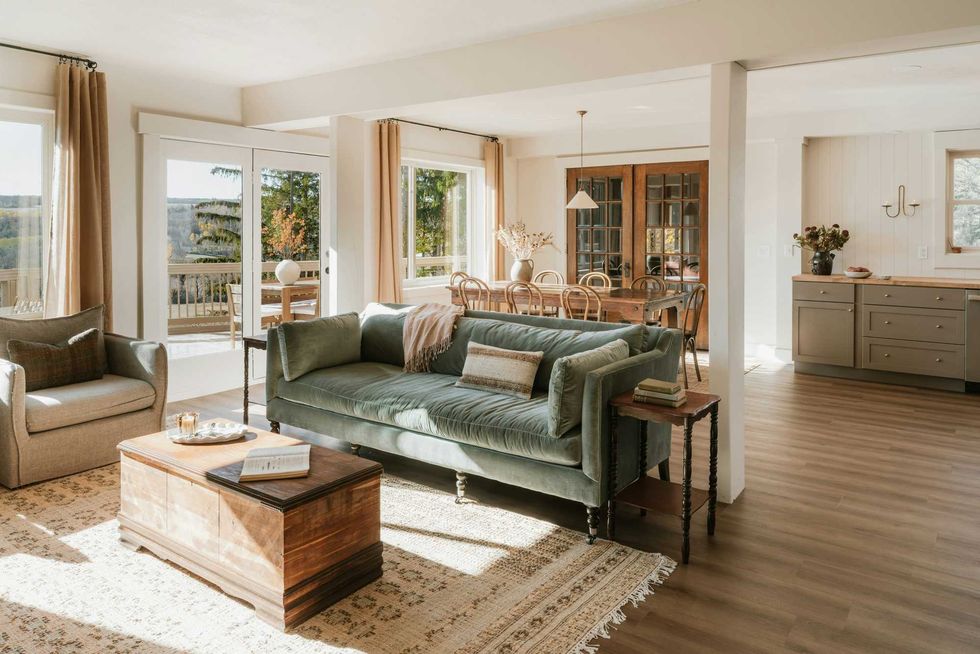 Spacious living room with a green sofa, wooden coffee table, and dining area in sunlight.
