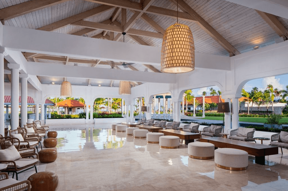 Spacious resort lobby with wicker chairs, plush stools, and large pendant lights.