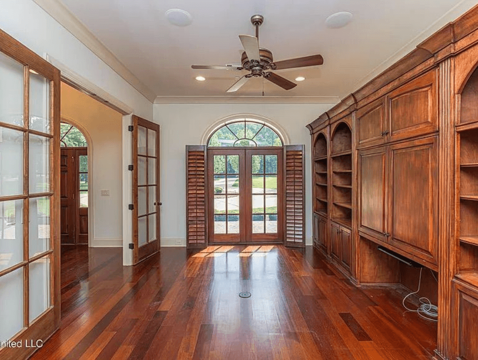 Spacious room with wooden shelves, French doors, and a ceiling fan.