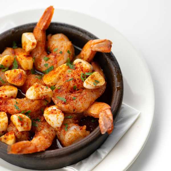 Spicy shrimp with garlic and herbs in a black bowl on a white plate.