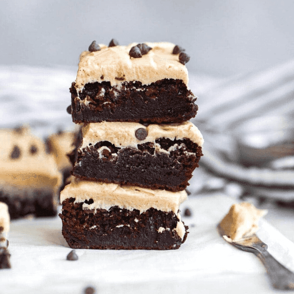 Stack of chocolate brownies with frosting and chocolate chips on top.