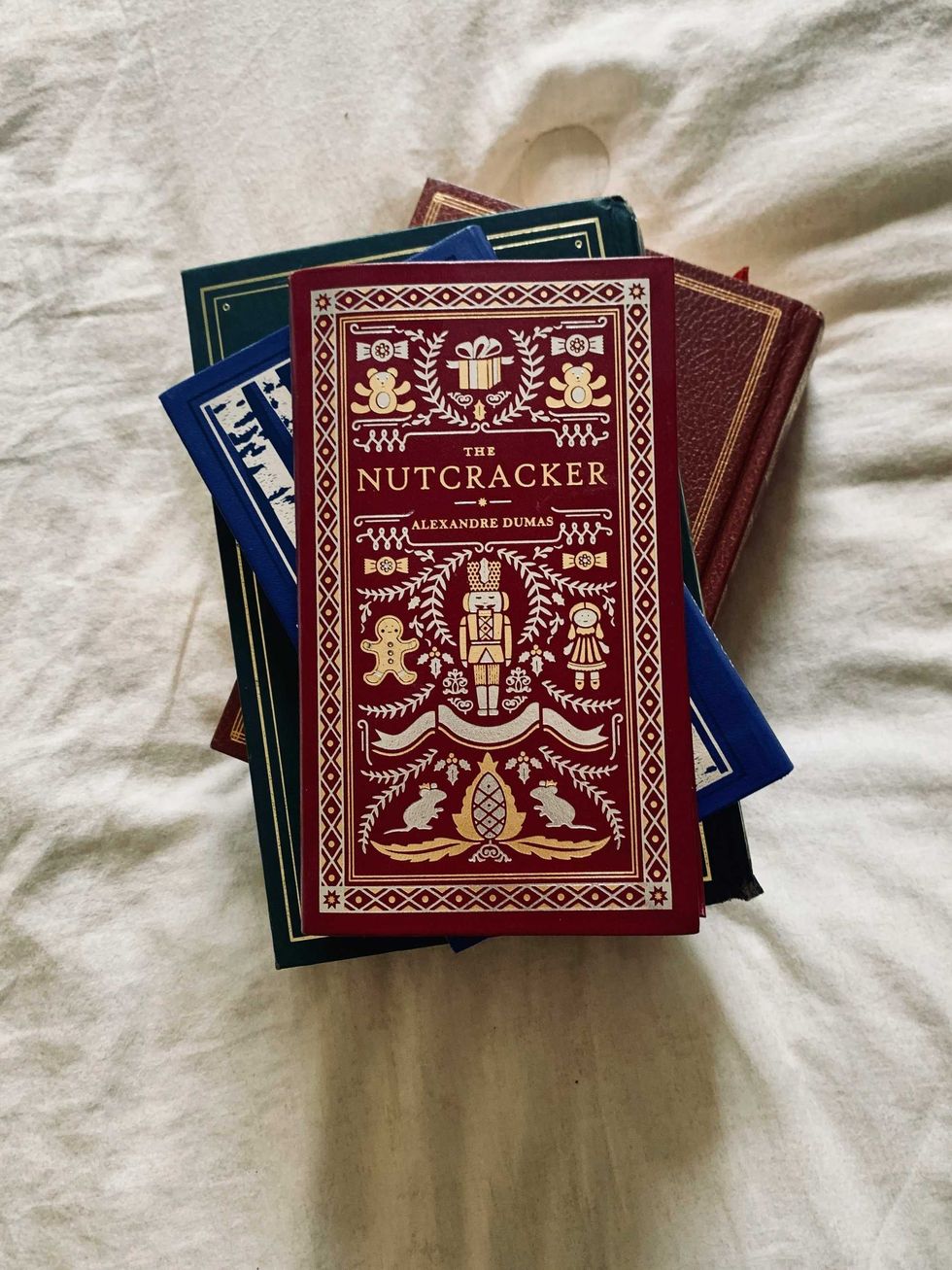 Stack of classic books, top one is "The Nutcracker" by Alexandre Dumas on a beige fabric.