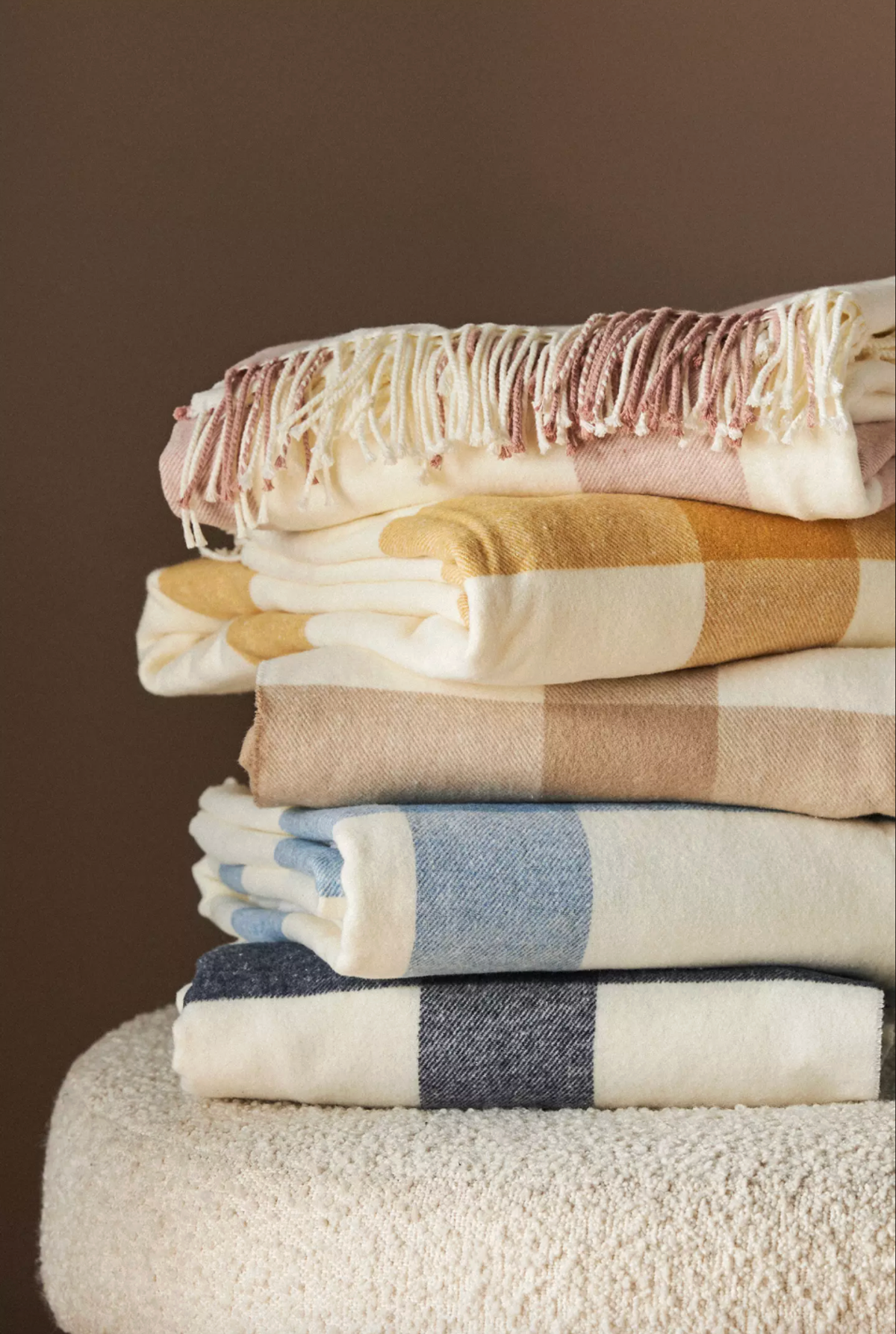 Stack of cozy, plaid blankets in soft colors on a textured surface.