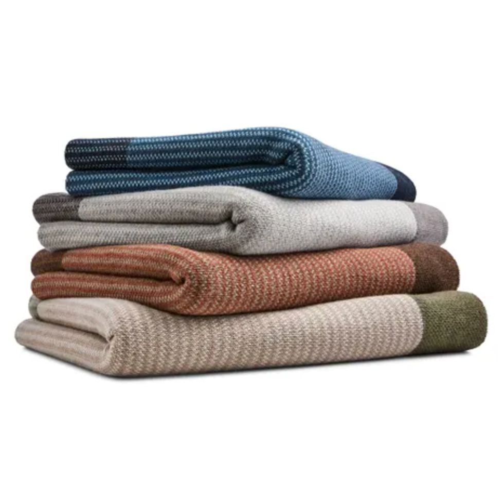 Stack of folded, multicolored knit blankets in blue, gray, orange, and beige.