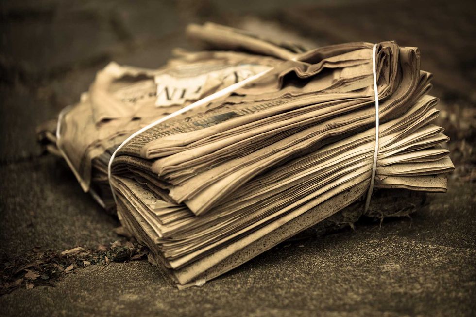 Stack of old, yellowed newspapers bound with string on a stone surface.