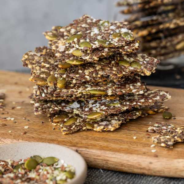 Stack of seed crackers on a wooden board with scattered seeds.