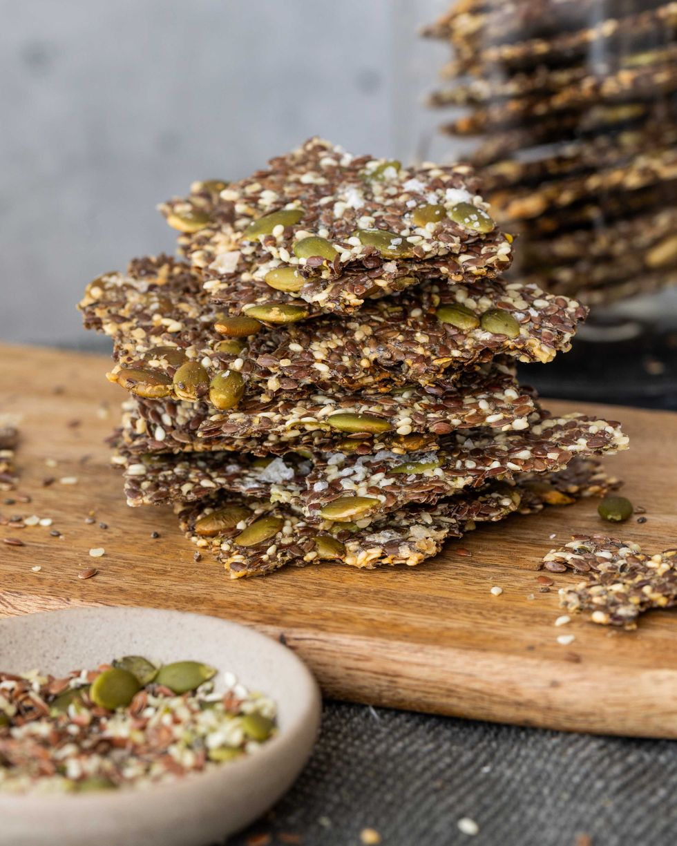 Stack of seed crackers on a wooden board with scattered seeds.
